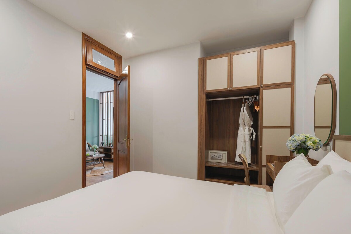 A bedroom with a bed, a wooden wardrobe, a mirror, and a door leading to another room.