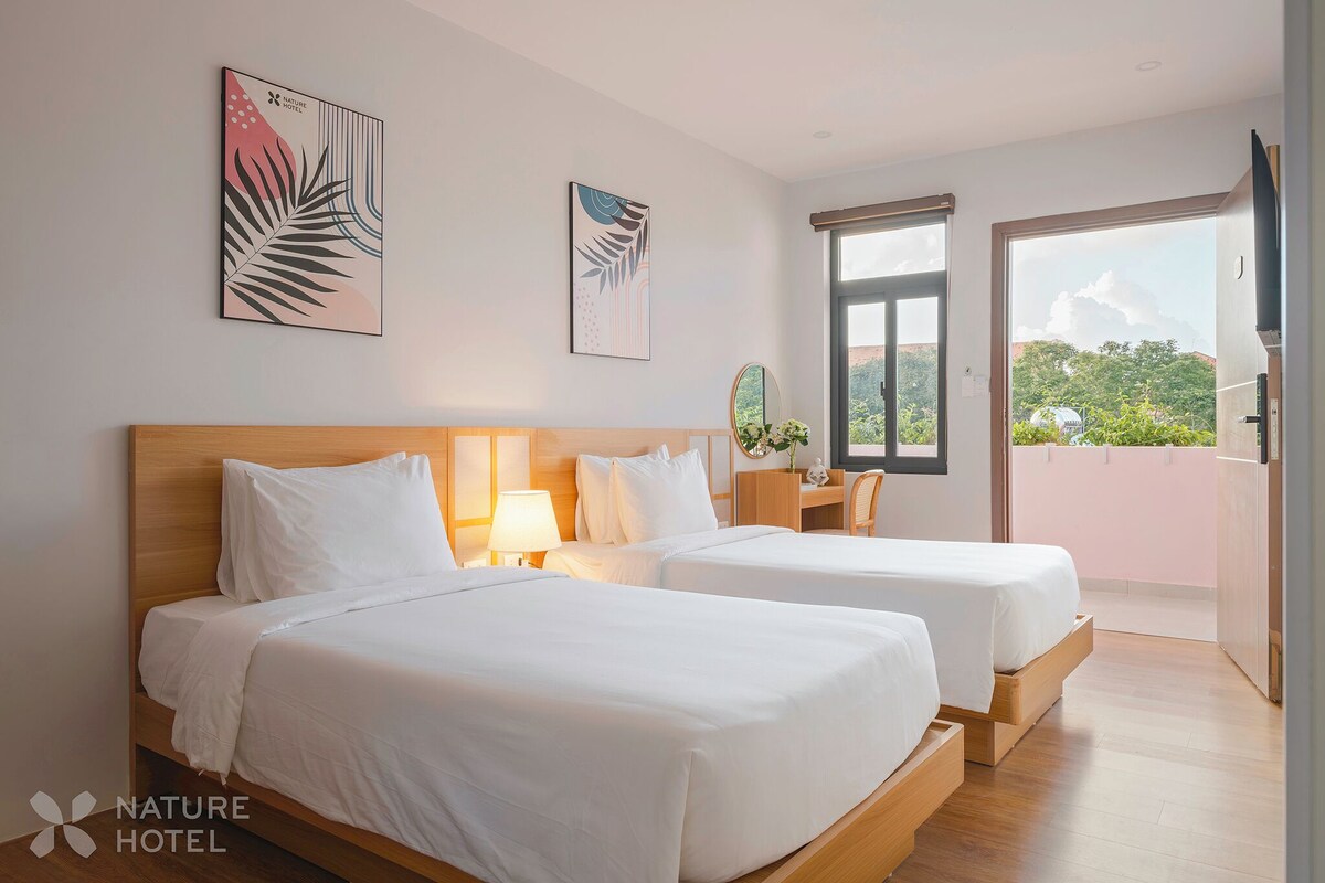 A hotel room with two beds, a desk, a chair, a TV, and a balcony with a view.