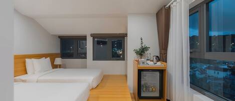 A hotel room with two beds, a small refrigerator, a window with curtains, and a view of the city at night.