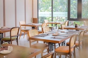 A hotel dining area with wooden tables and chairs, a view of greenery outside, and a sign indicating the hotel's name. - Nature Hotel - Le Hong Phong (Da Lat)