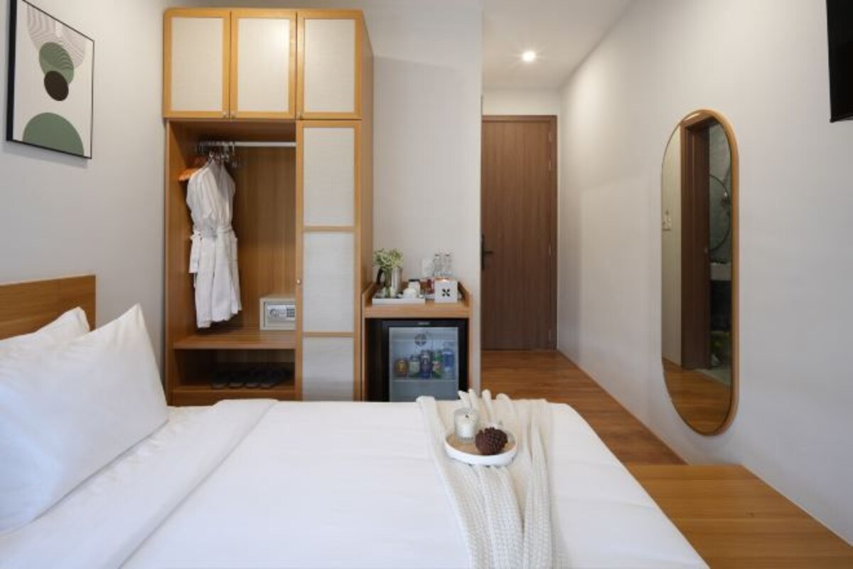 A hotel room with a bed, a wardrobe, a small fridge, a mirror, and a tray with items on the bed.