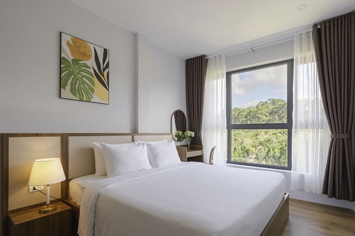 A hotel room with a large bed, a bedside lamp, a mirror, and a window with curtains.