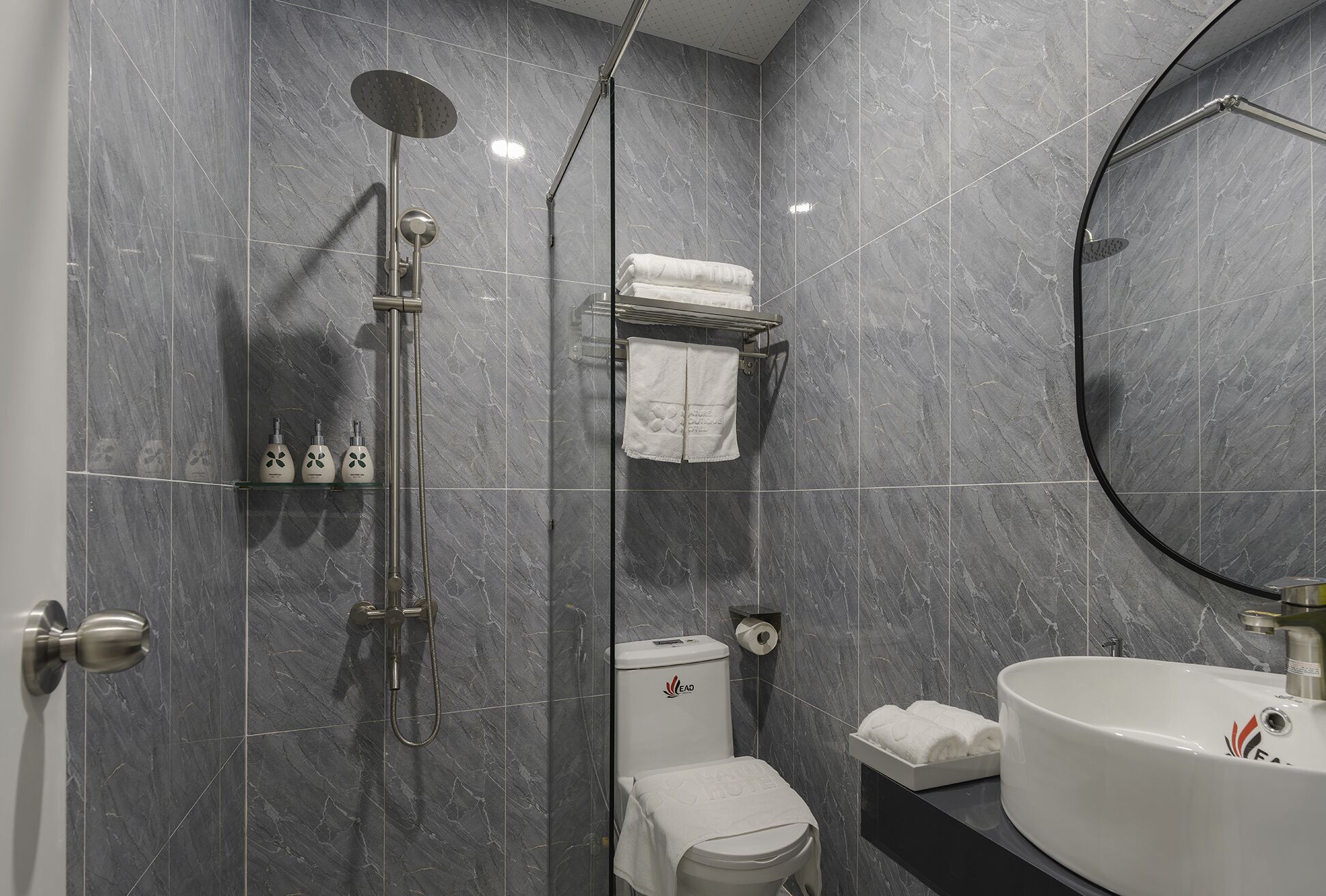 A modern bathroom with grey marble tiles, a walk-in shower, a toilet, a sink, and a mirror.