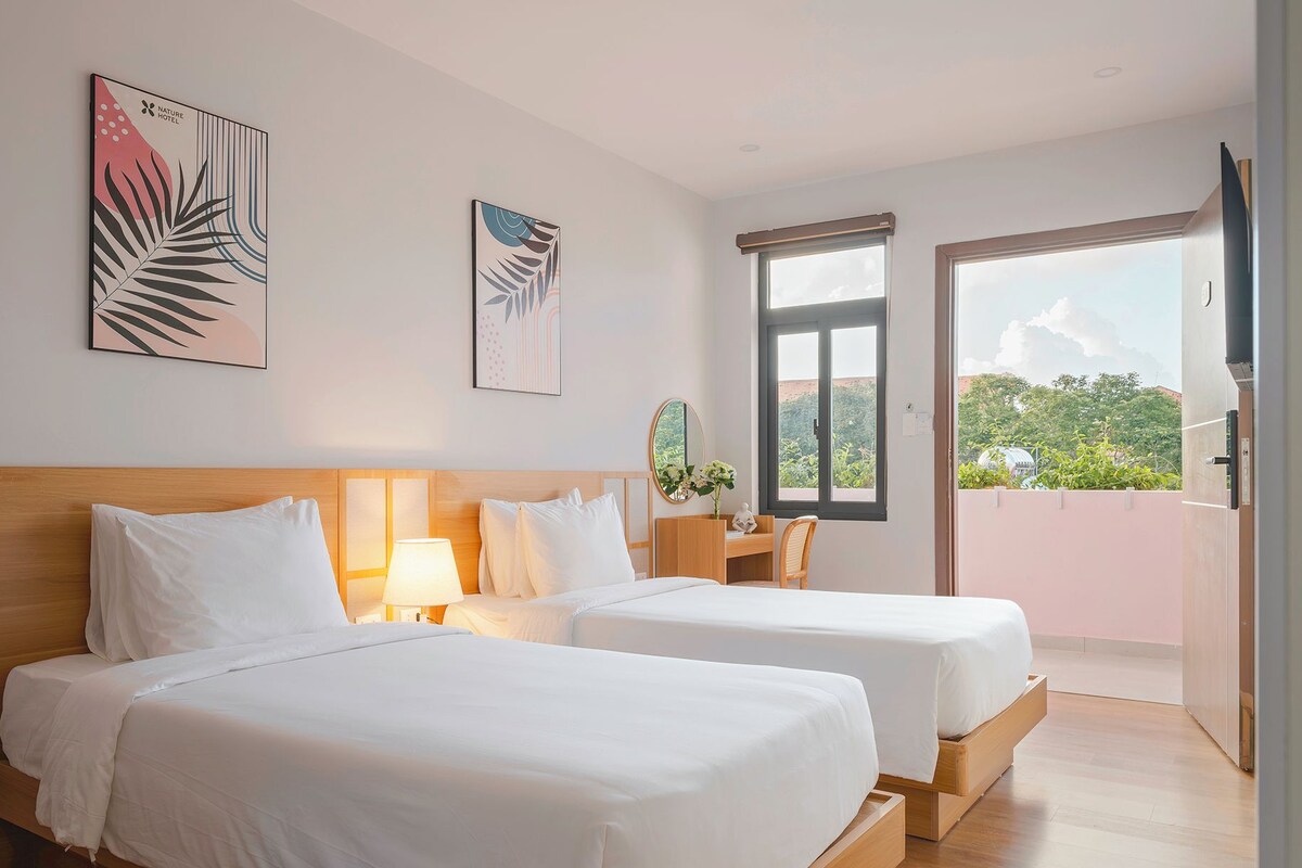A hotel room with two beds, a desk, a chair, a TV, and a balcony with a view.