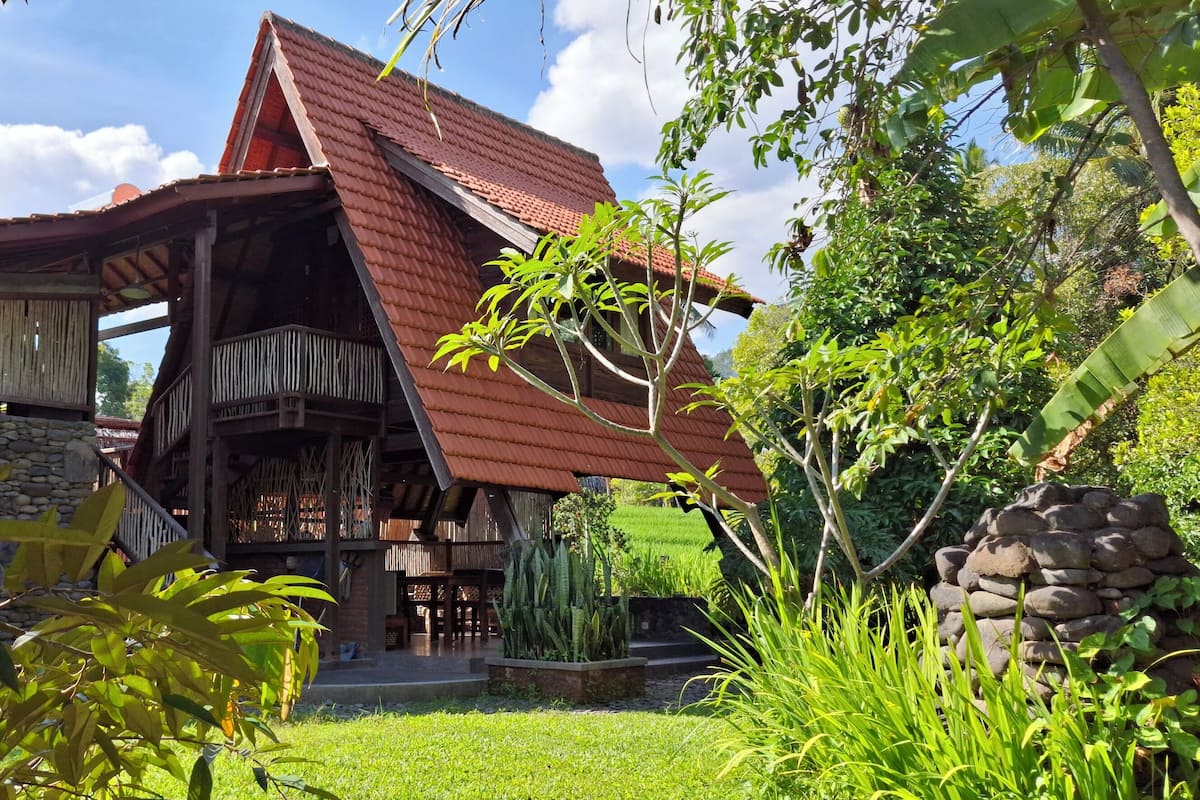 A rustic house with a sloped roof, surrounded by lush greenery and a well-maintained garden.