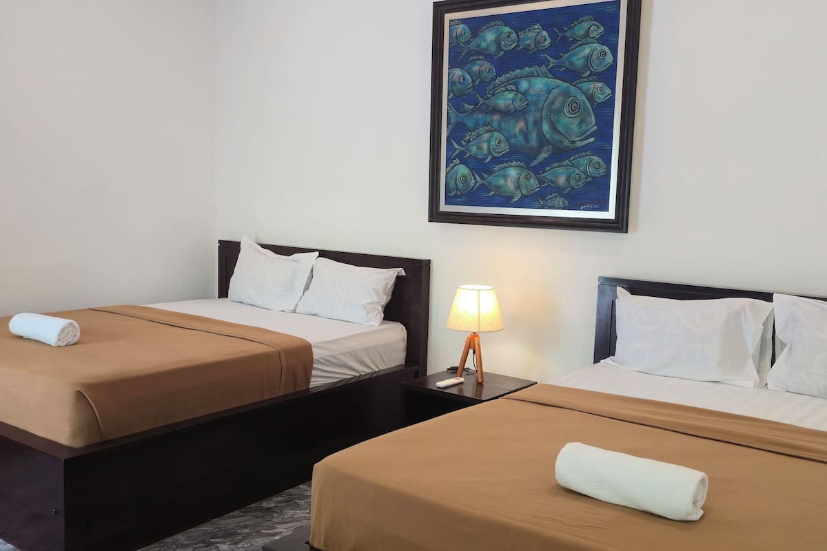 A hotel room with two beds, each with a brown bedspread and white pillows. There is a framed artwork above the beds, a nightstand with a lamp, and a marble floor.