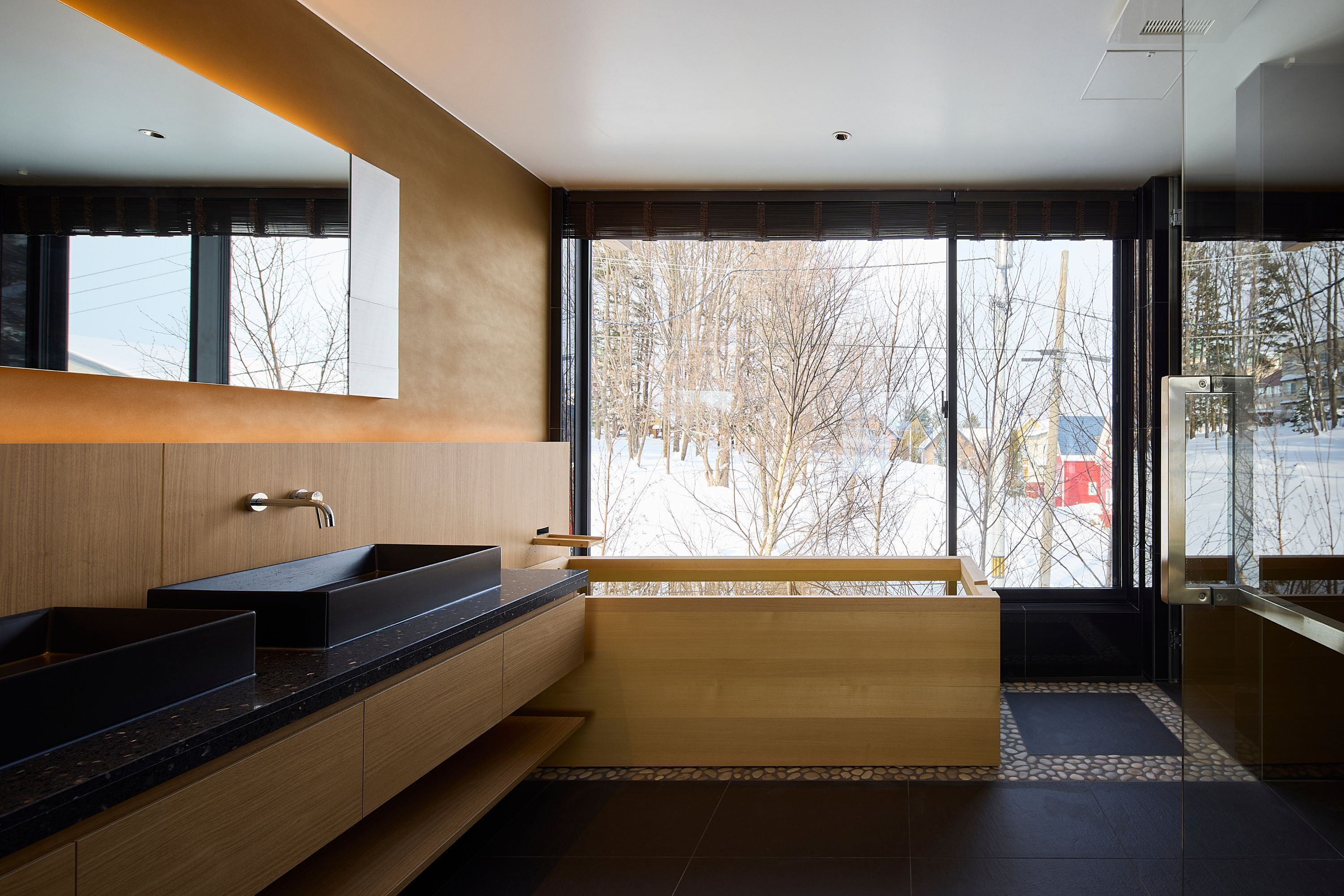 Un baño moderno con un ventanal grande, un tocador de madera y un lavamanos negro.