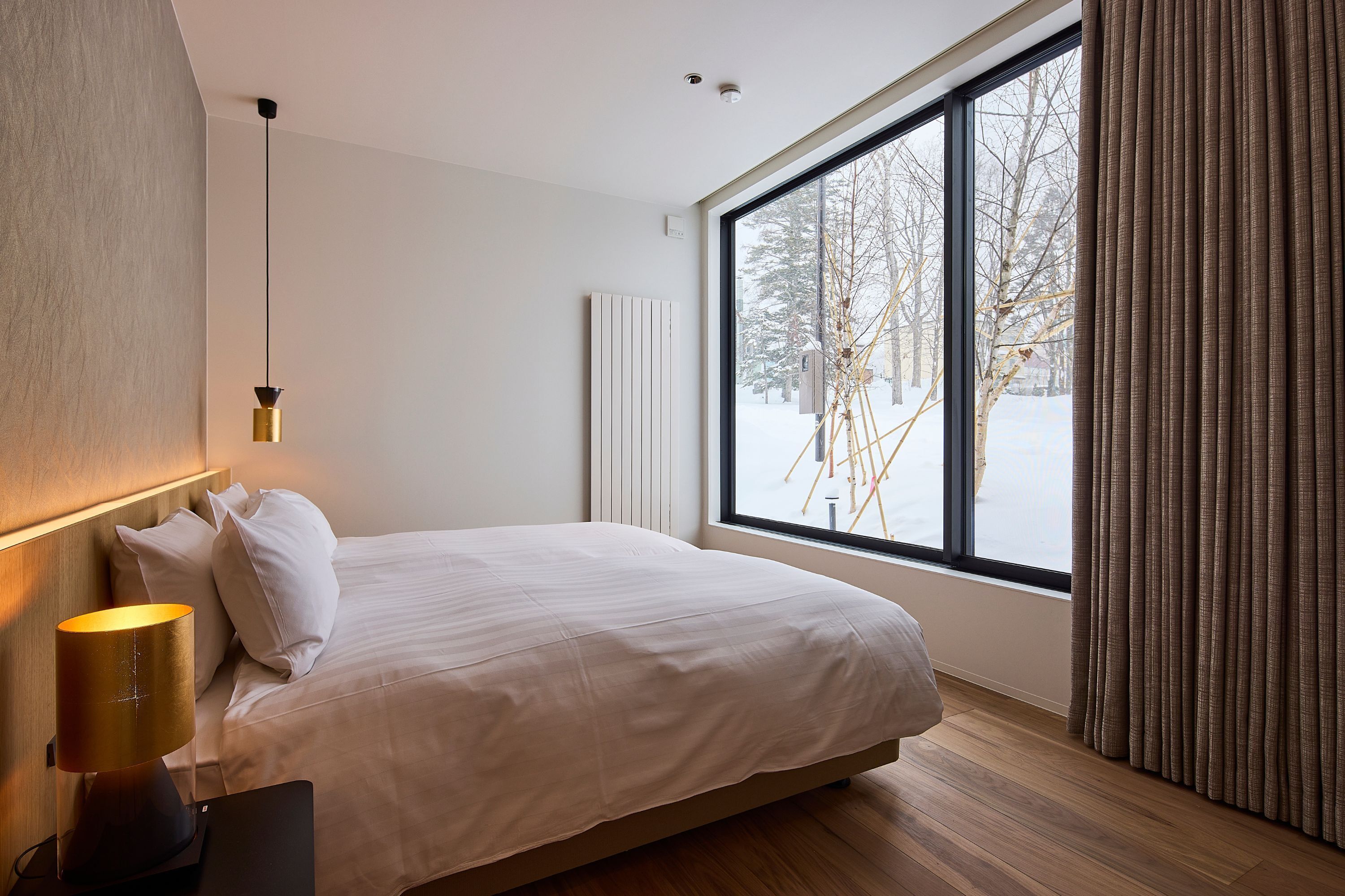 A modern bedroom with a large window, a bed, and a bedside lamp.