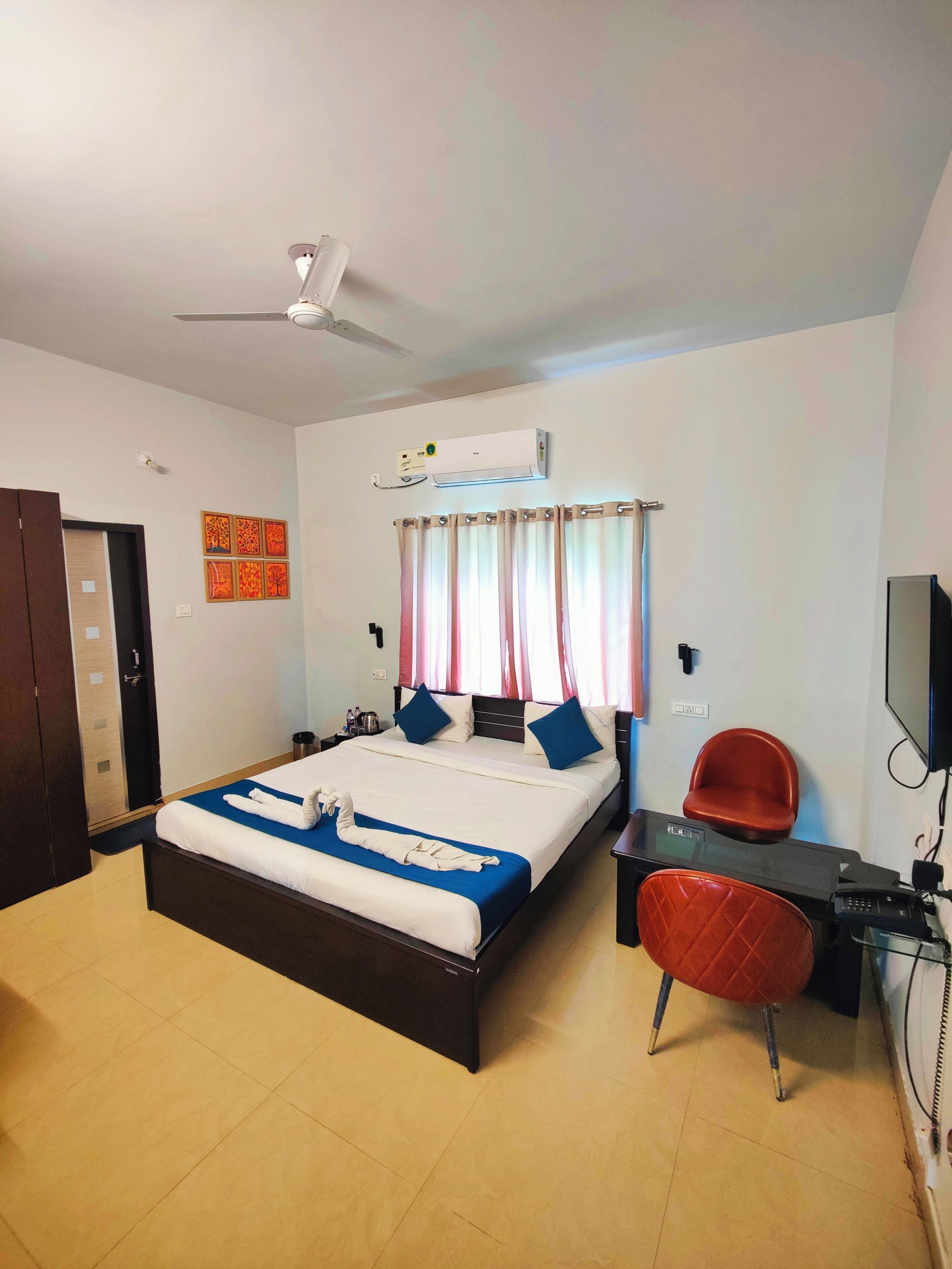 Une chambre d’hôtel équipée d’un lit, d’un bureau, d’une chaise, d’un climatiseur, d’une télévision et d’un ventilateur de plafond.