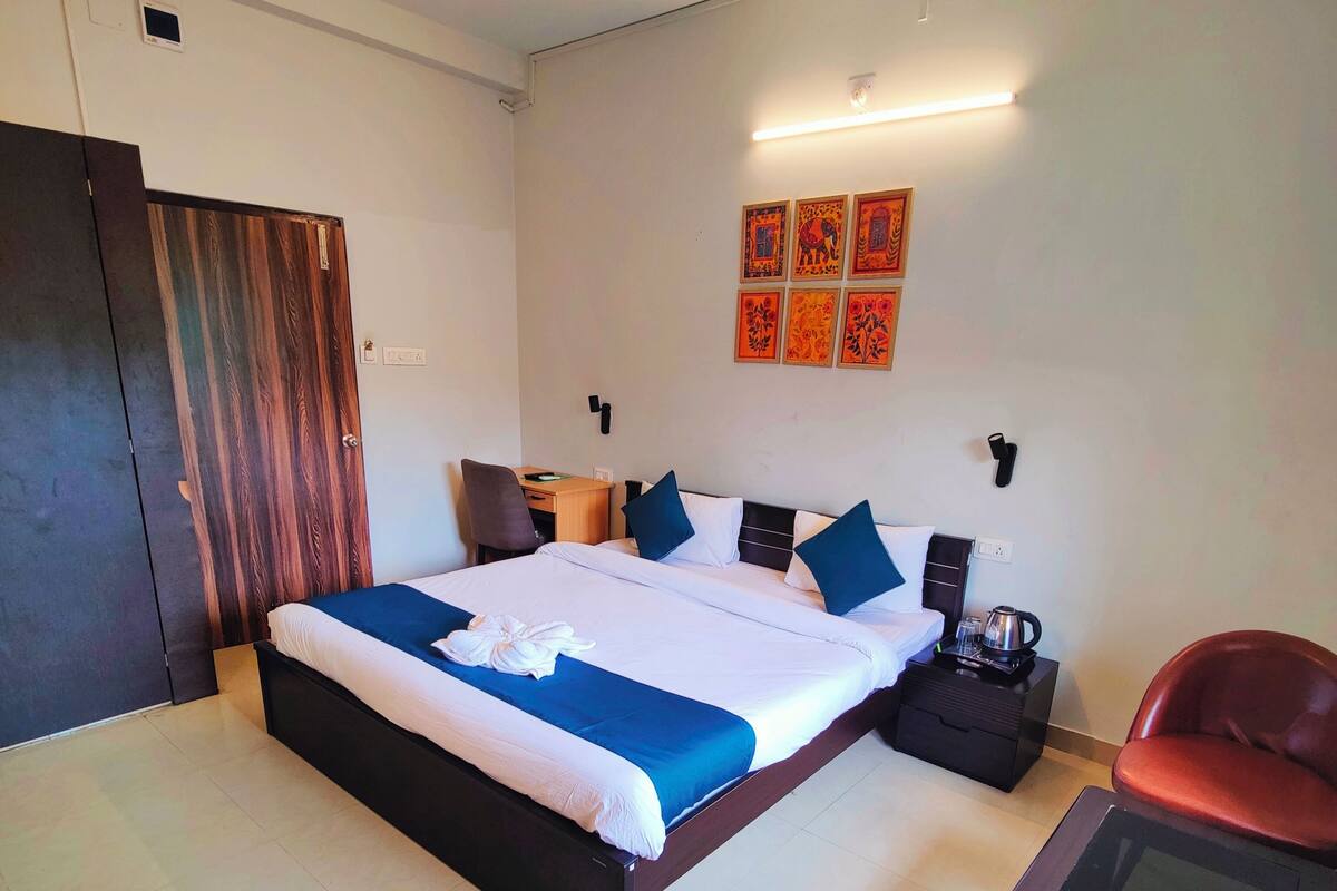 Quarto de hotel com uma cama grande, uma escrivaninha, uma cadeira e uma mesa pequena.