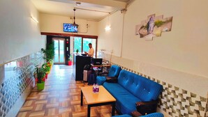 A hotel lobby with a blue sofa, wooden flooring, a reception desk, and a TV screen. - The Nook (Bhubaneshwar)