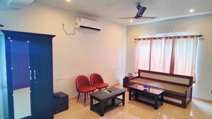 A spacious living room with a sofa set, two red chairs, a coffee table, and a ceiling fan. - The Nook (Bhubaneshwar)