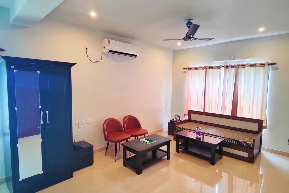 Uma sala de estar ampla com sofá, duas poltronas vermelhas, mesa de centro e ventilador de teto.