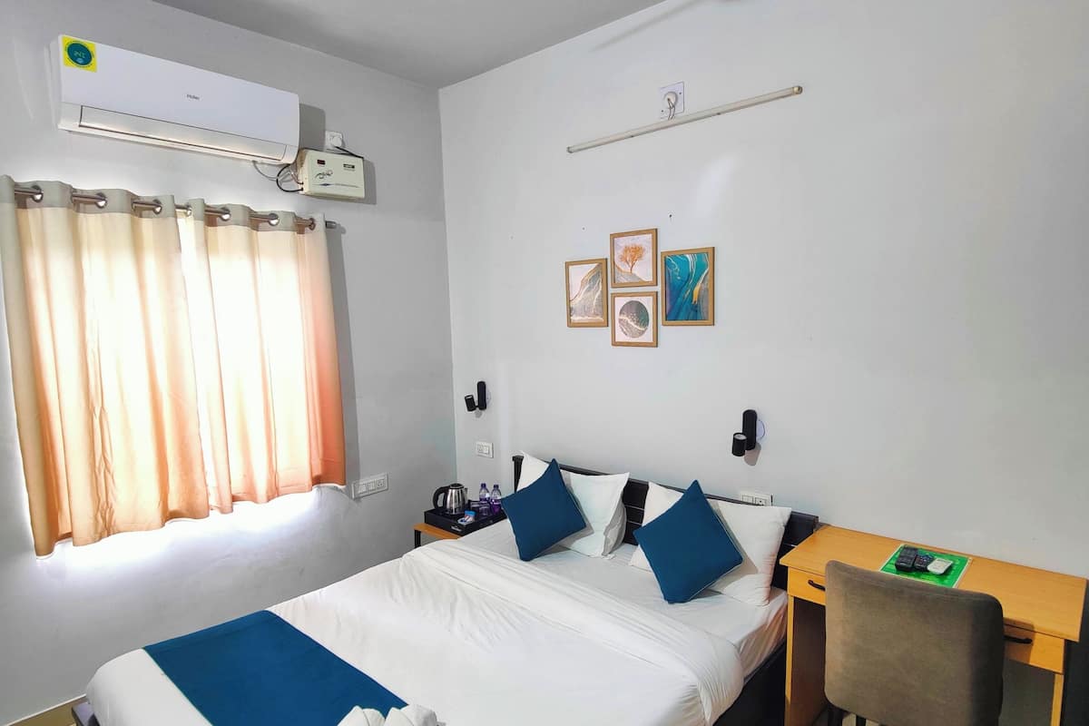Quarto de hotel com cama, escrivaninha, cadeira, ventilador de teto, ar condicionado e janela com cortinas.