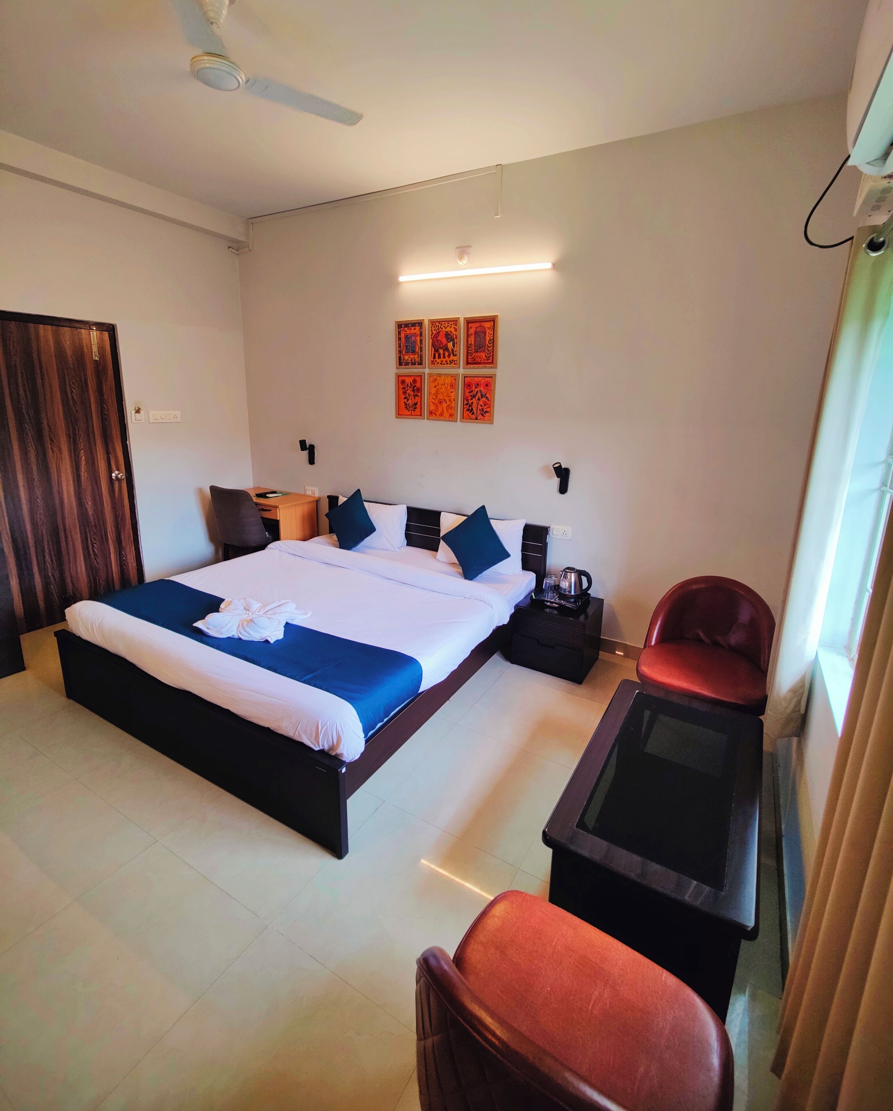 A hotel room with a large bed, a desk, a chair, a small table, and a ceiling fan.