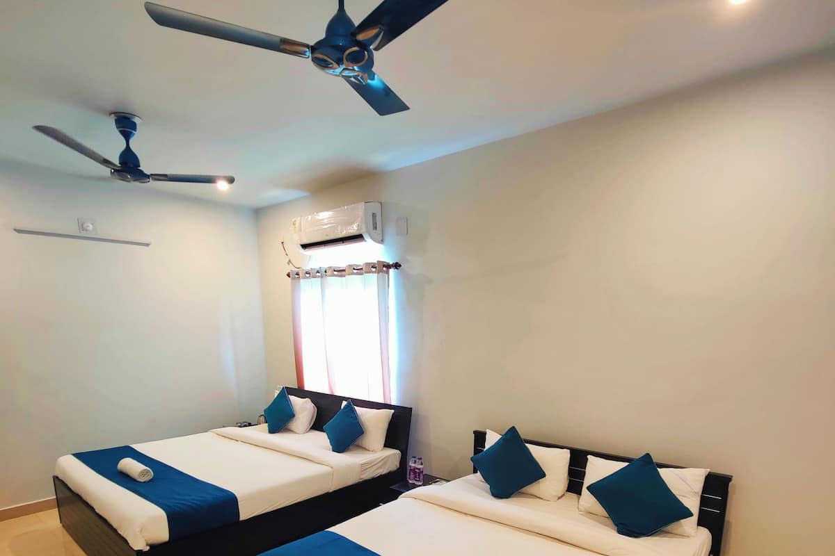 Quarto de hotel com duas camas, ventoinha no teto, ar condicionado e janela com cortinas.
