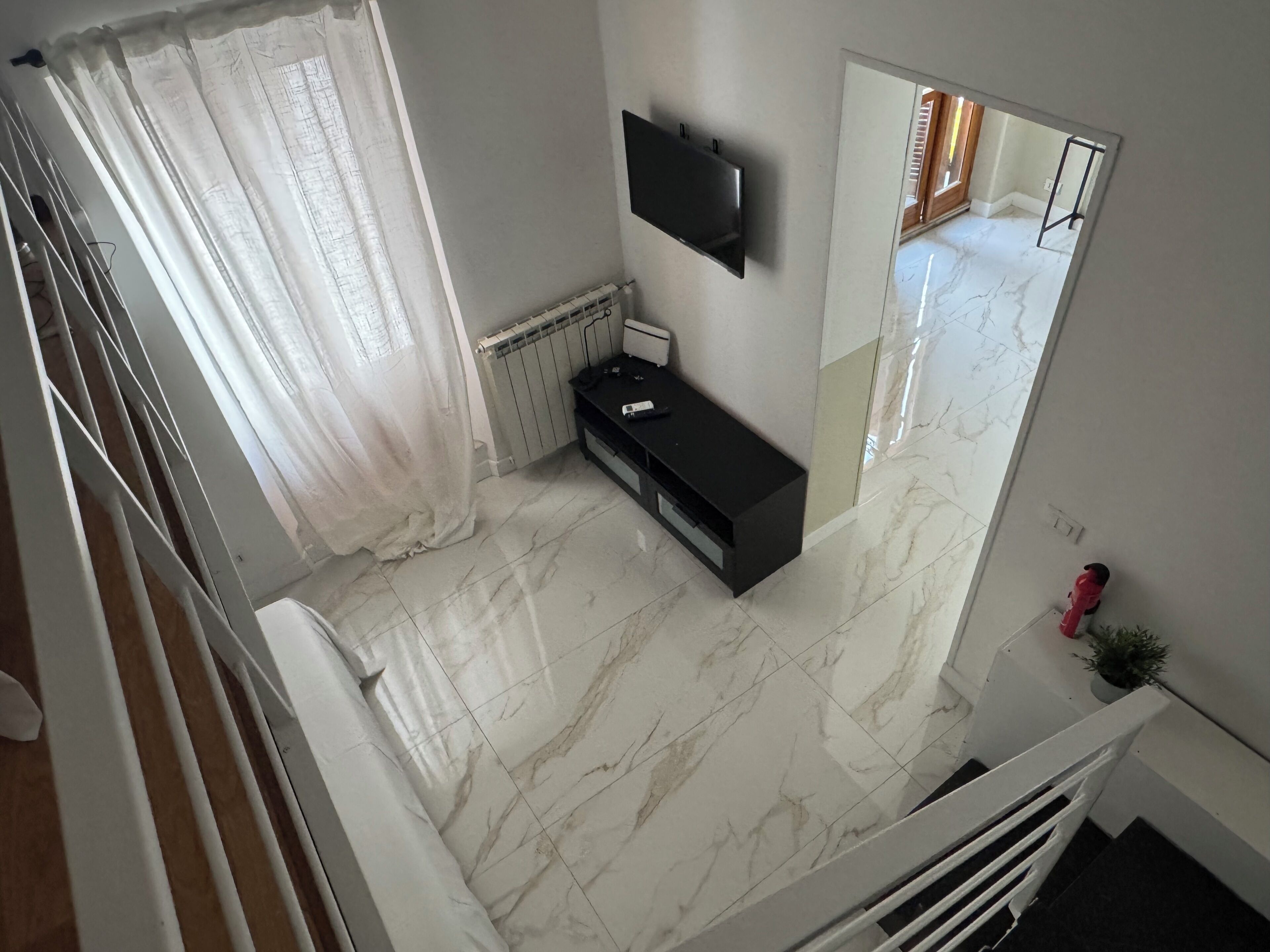 A room with a marble floor, a black TV mounted on the wall, a white radiator, and a white curtain.