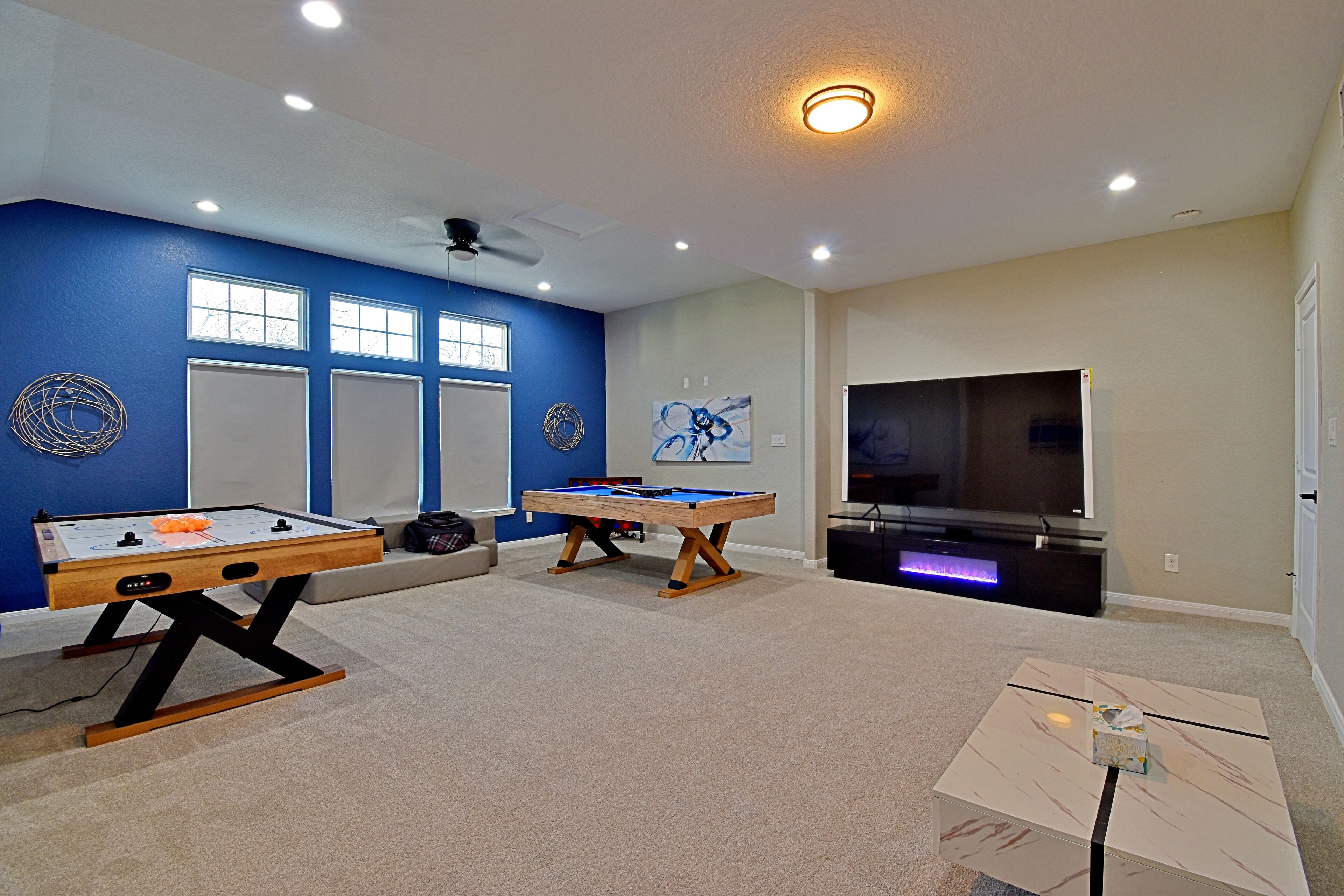 Una habitación con dos mesas de futbolín, un televisor de pantalla plana grande y un ventilador de techo.