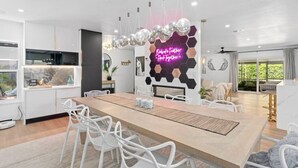 A modern kitchen with a dining area, a neon sign, and a view of greenery outside.