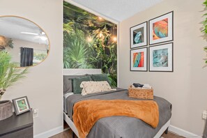 A bedroom with a bed, a mirror, a wall mural, and framed pictures.