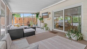 An outdoor patio with a sofa, a dining table, and a TV mounted on the wall.