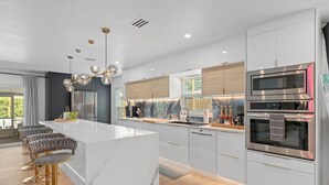 A modern kitchen with a marble island, stainless steel appliances, and bar stools.