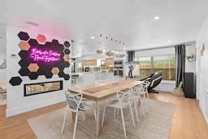 Una cocina moderna con armarios blancos, una zona de comedor con una mesa de madera y sillas blancas, y un letrero de neón en la pared.