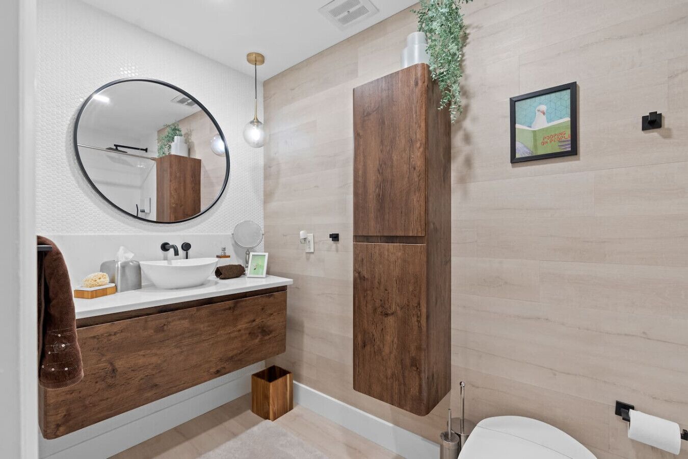Une salle de bain moderne avec un grand miroir rond, un meuble-lavabo en bois, un lavabo blanc et des toilettes.
