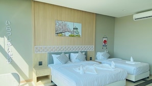 Een hotelkamer met twee bedden, een houten hoofdeinde, een wandairconditioner en een ingelijste foto boven de bedden.