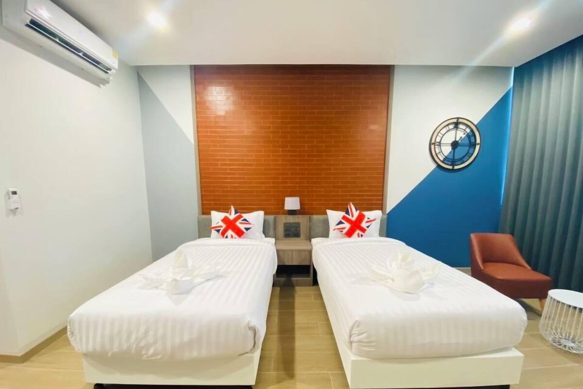 A hotel room with two beds, a wooden accent wall, a clock, and a red chair.