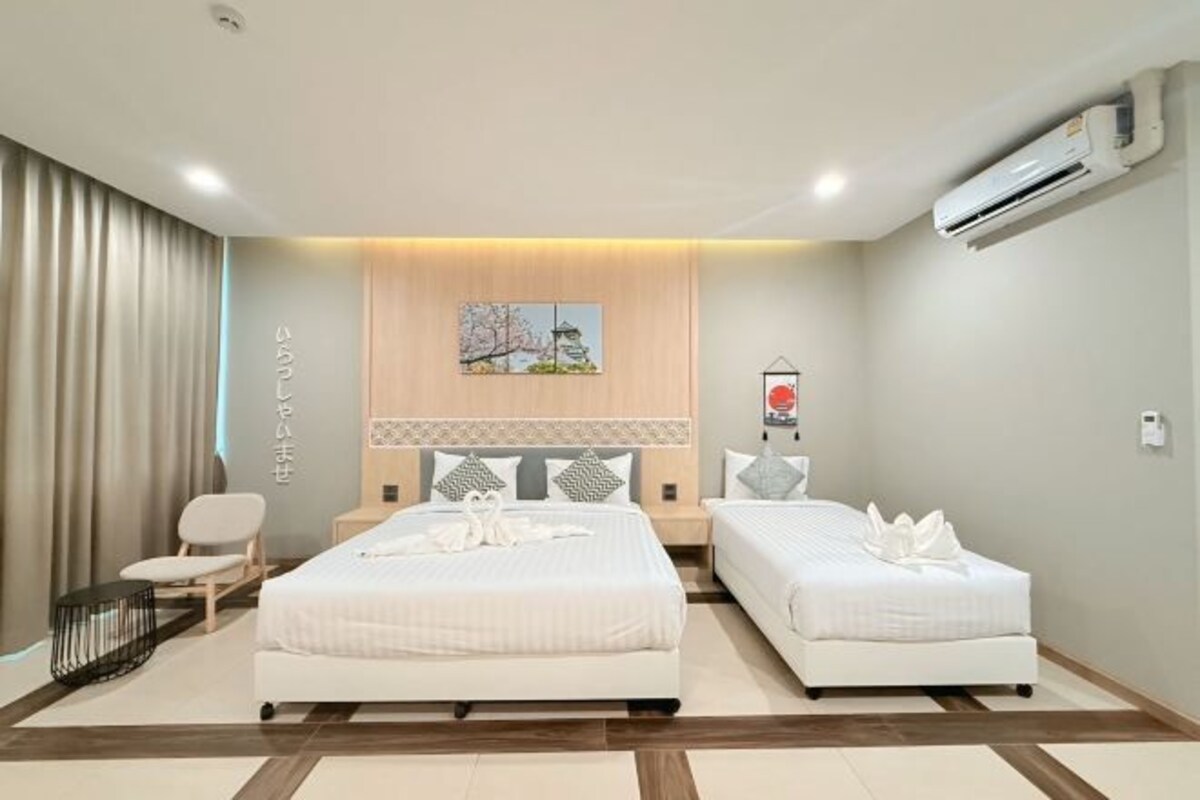A hotel room with two beds, a wooden headboard, a wall-mounted air conditioner, and a small table with a chair.