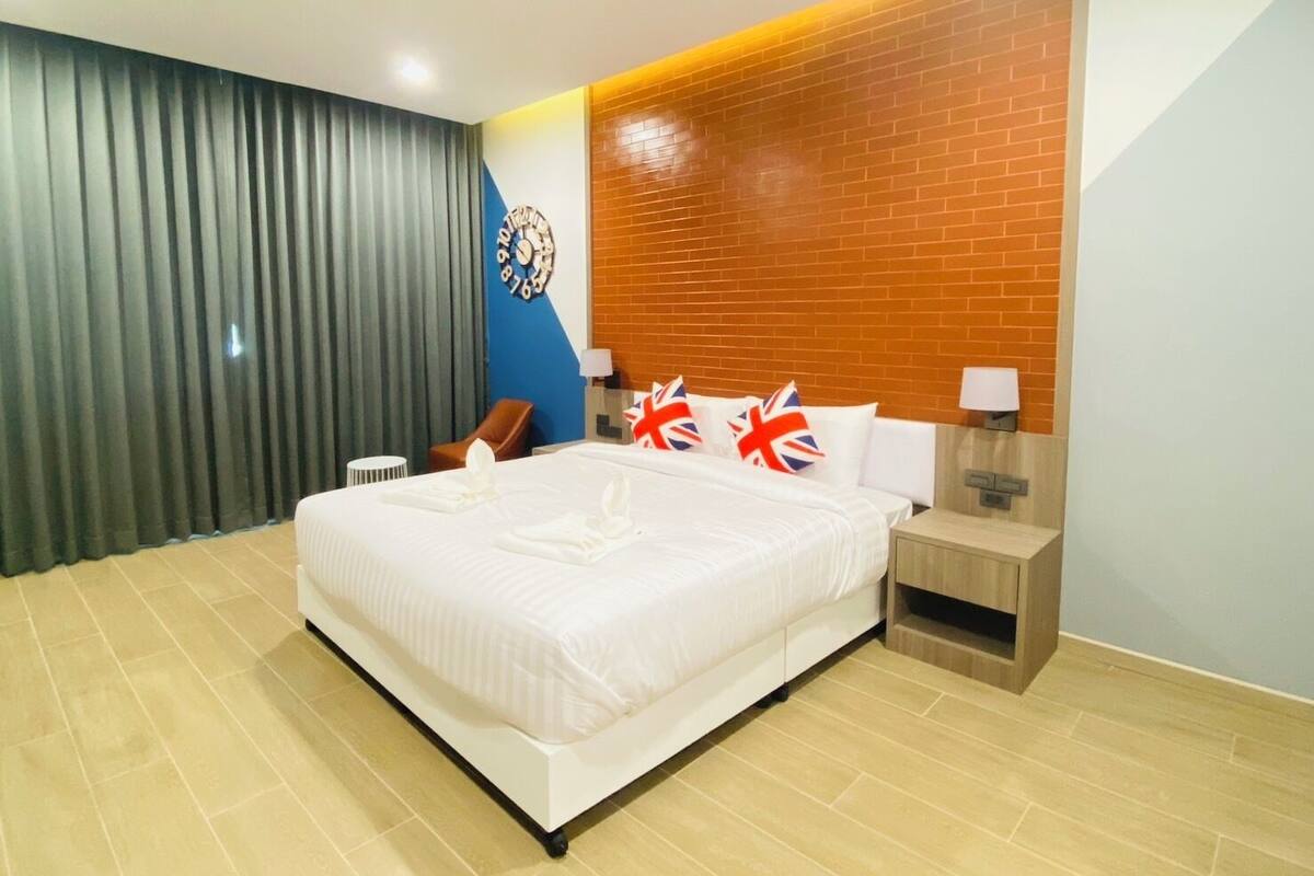 A hotel room with a large bed, a wooden headboard, a clock, and a British flag pillow.