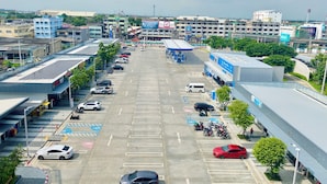 Een parkeerplaats met meerdere rijen geparkeerde auto's en motorfietsen, een tankstation en een groot gebouw met een blauw-witte gevel.