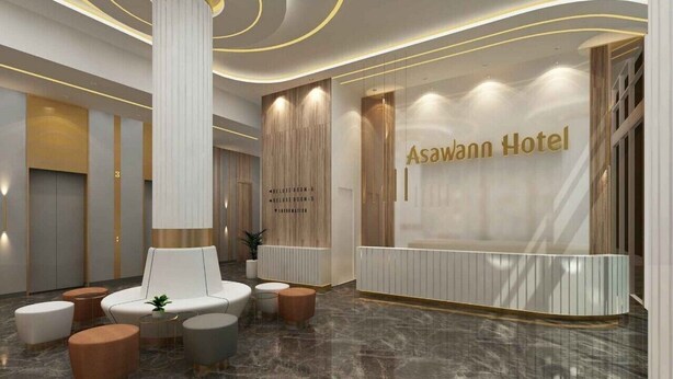 Een moderne hotellobby met een receptiebalie, een zithoek en een grote zuil.