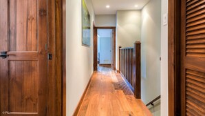 A wooden hallway with a door on the left, a staircase with a railing on the right, and a framed picture on the wall.