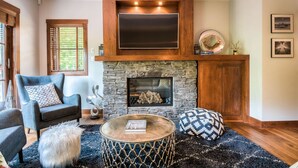 A living room with a stone fireplace, a mounted flat-screen TV, a comfortable sofa, and a round coffee table.