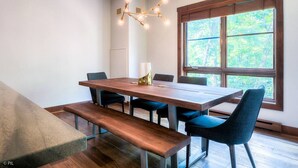 A dining area with a wooden table, blue upholstered chairs, a bench, and a pendant light.