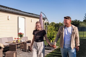 A couple walking hand in hand in a backyard with a patio, outdoor furniture, and a house in the background.