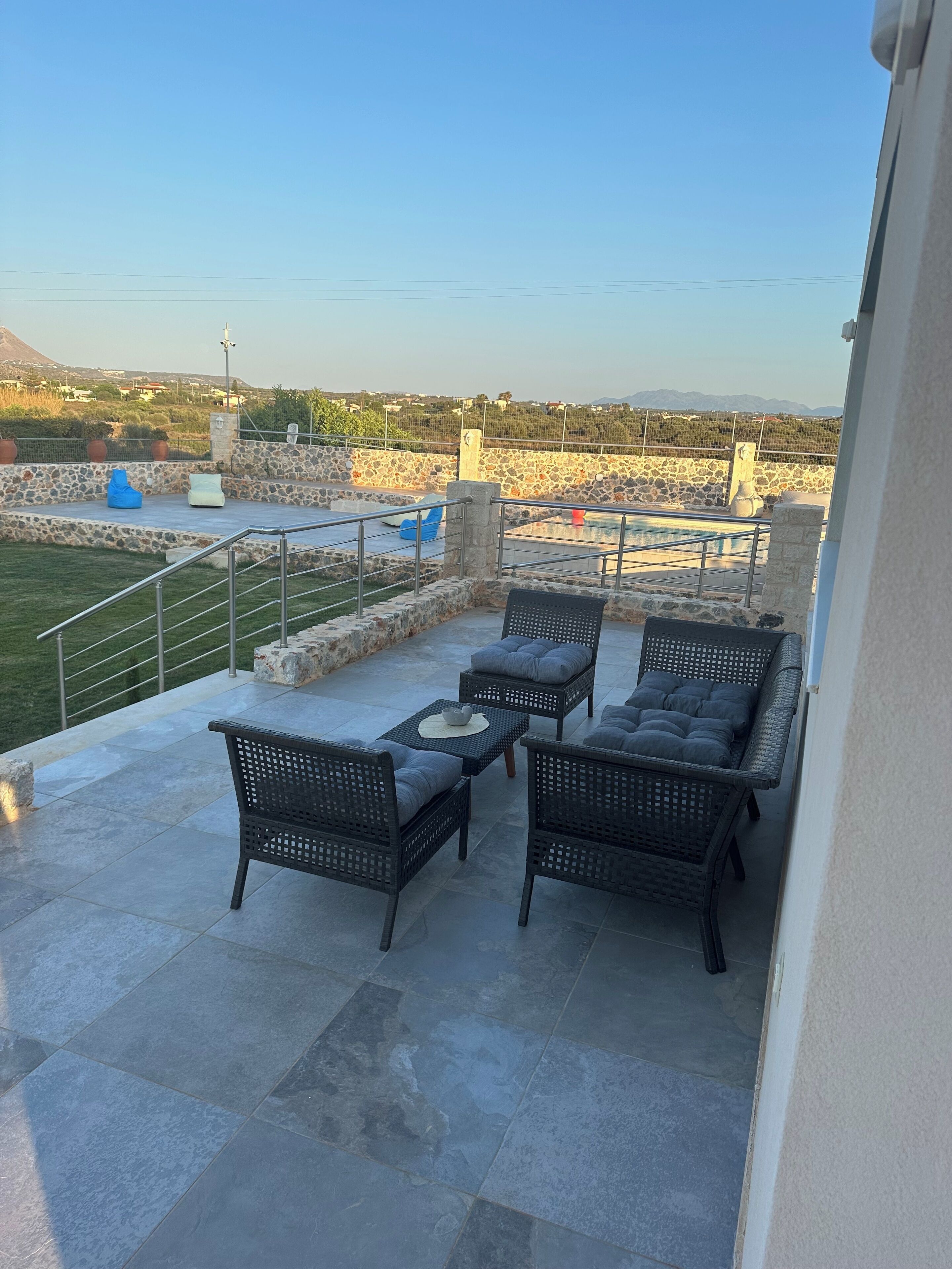 Eine Terrasse mit Korbmöbeln, einer Steinmauer und Blick auf einen Pool sowie die Ferne.