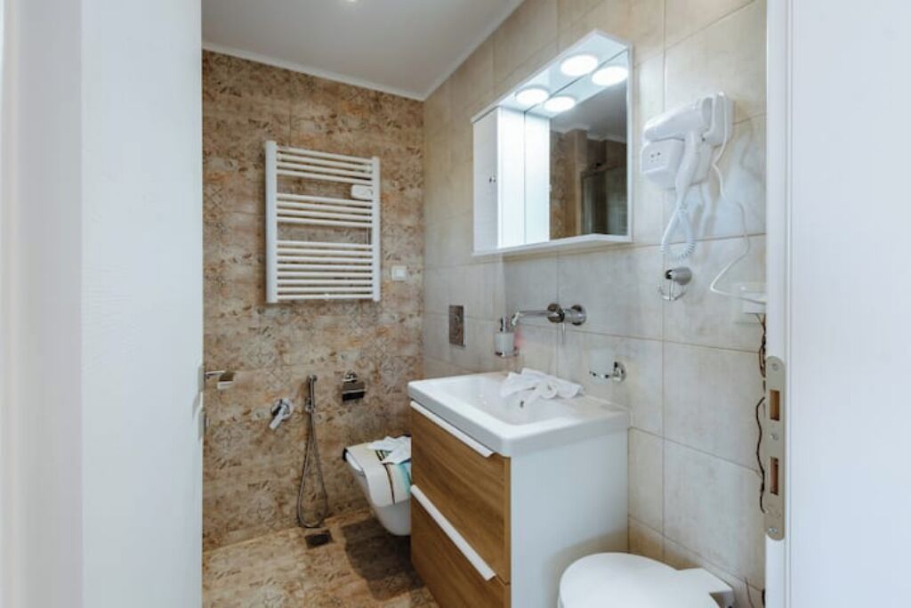 Un baño con lavamanos blanco, espejo y toallero.