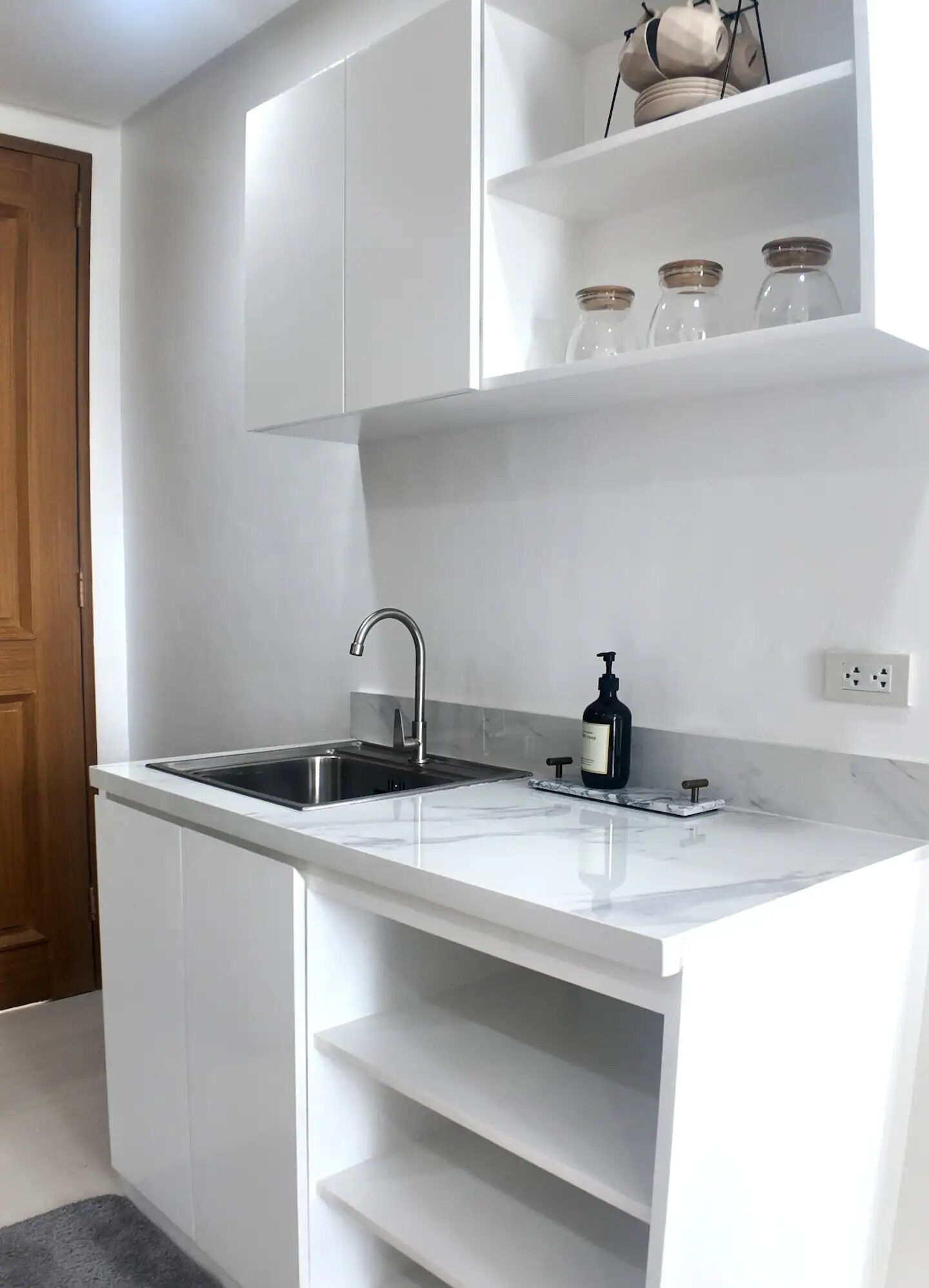 Una cuina moderna amb armaris blancs, un vàter d'acer inoxidable i un taulell de marbre.