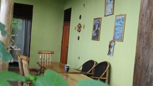 A dining area with a wooden table and chairs, a window with blinds, and wall decorations including framed pictures and a poster. - Kibale Eco Home  (Kibale)