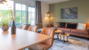 A modern living room with a sofa, chairs, a coffee table, and a dining table. There is a large window with curtains, a wall-mounted light, and a piece of abstract art. - Holiday Home Near Biesbosch & Breda (Oosterhout)