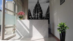 Un espace d’accueil doté d’un comptoir en marbre, d’une plante en pot et d’une fresque murale représentant un temple.