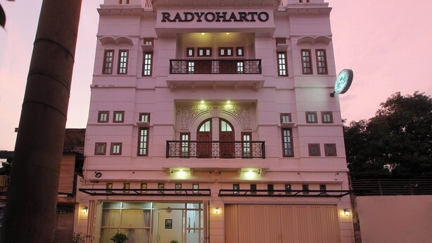 Un bâtiment sur lequel le nom RADYOHARTO est clairement affiché. Il présente une façade symétrique avec une entrée centrale, des balcons et une horloge sur le côté droit.
