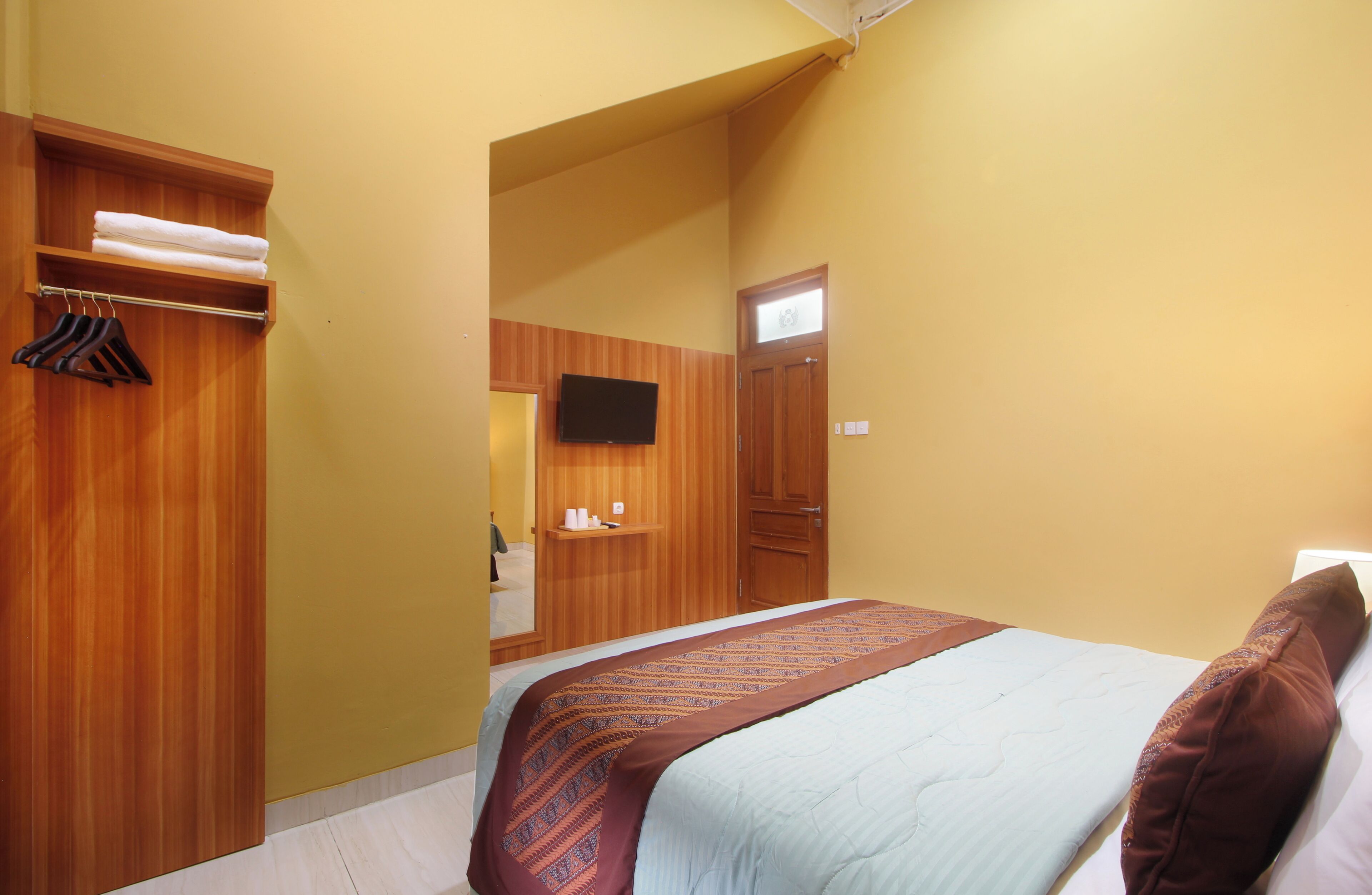 A bedroom with a bed, a wooden wardrobe, a television, and a bathroom visible in the background.
