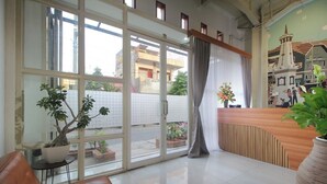 Un espace d’accueil avec un bureau en bois, un canapé en cuir marron et une grande fenêtre donnant sur la rue et les bâtiments.