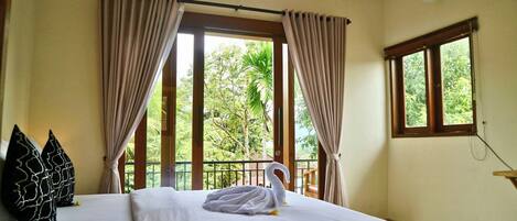 Habitación de hotel con dos camas, cortinas color beige, un balcón y vistas a zonas verdes, y un equipo de aire acondicionado.