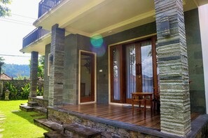 A house with a wooden deck, stone pillars, and a balcony. - Gria Sindhu Homestay Sidemen (Sidemen)