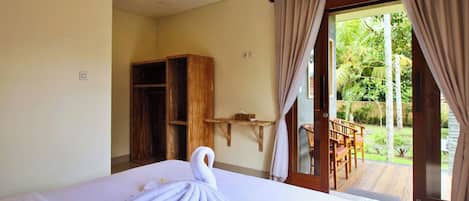 A bedroom with a bed, a wooden wardrobe, a small table, and a view of an outdoor area with a patio and chairs.